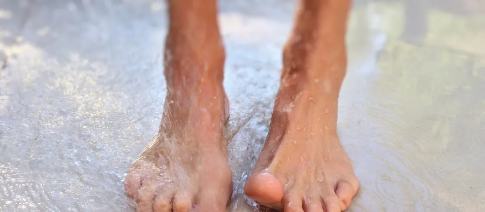 Bare feet cooling in shallow water on the sand.