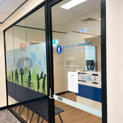 The clinic's glass door with the blue Burwood Podiatry logo, and the reception desk inside.