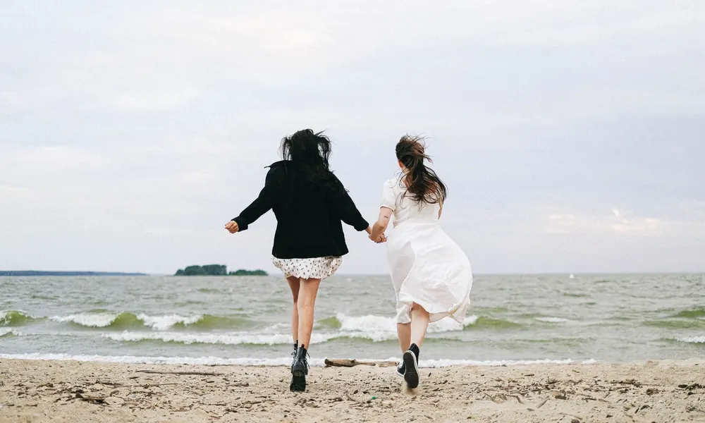 Two people running hand in hand towards the sea.