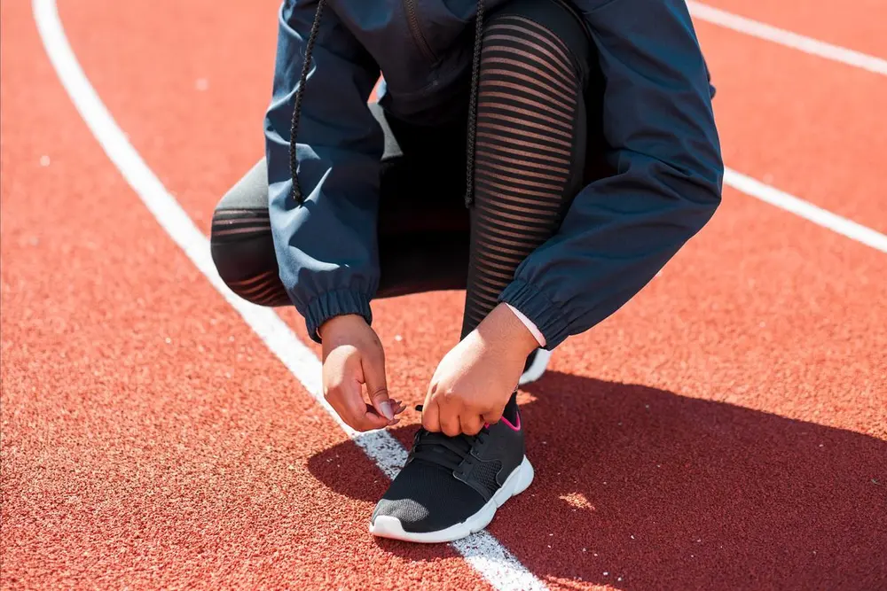 A person tying running shoes on an outdoor court.