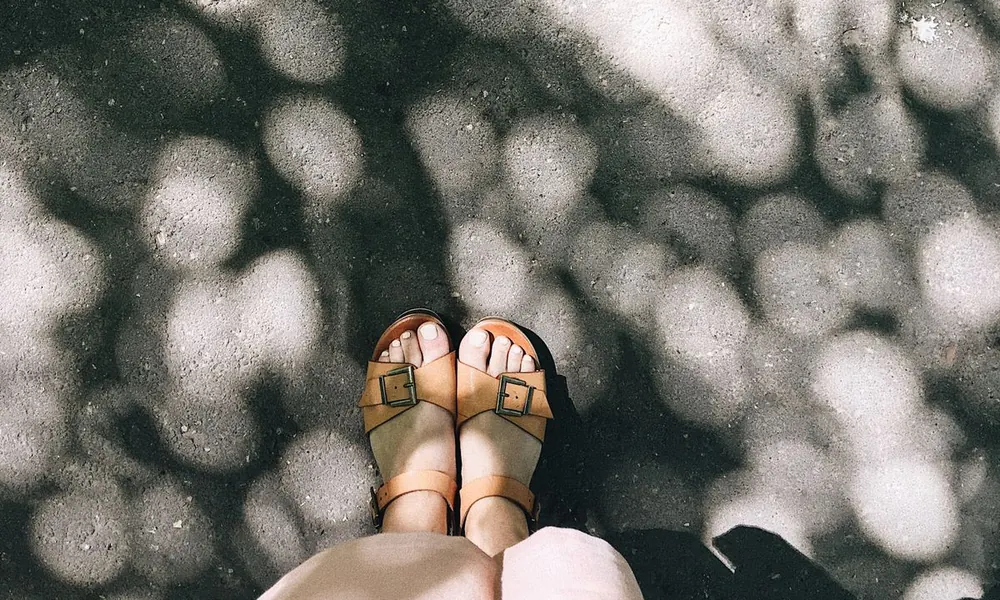Feet in sandals on a sunlit path.