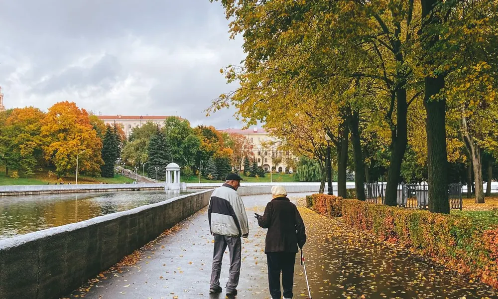 Two older adults walking together beside trees.